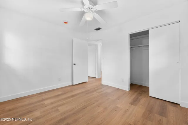 an empty room with wooden floor chandelier fan and closet area