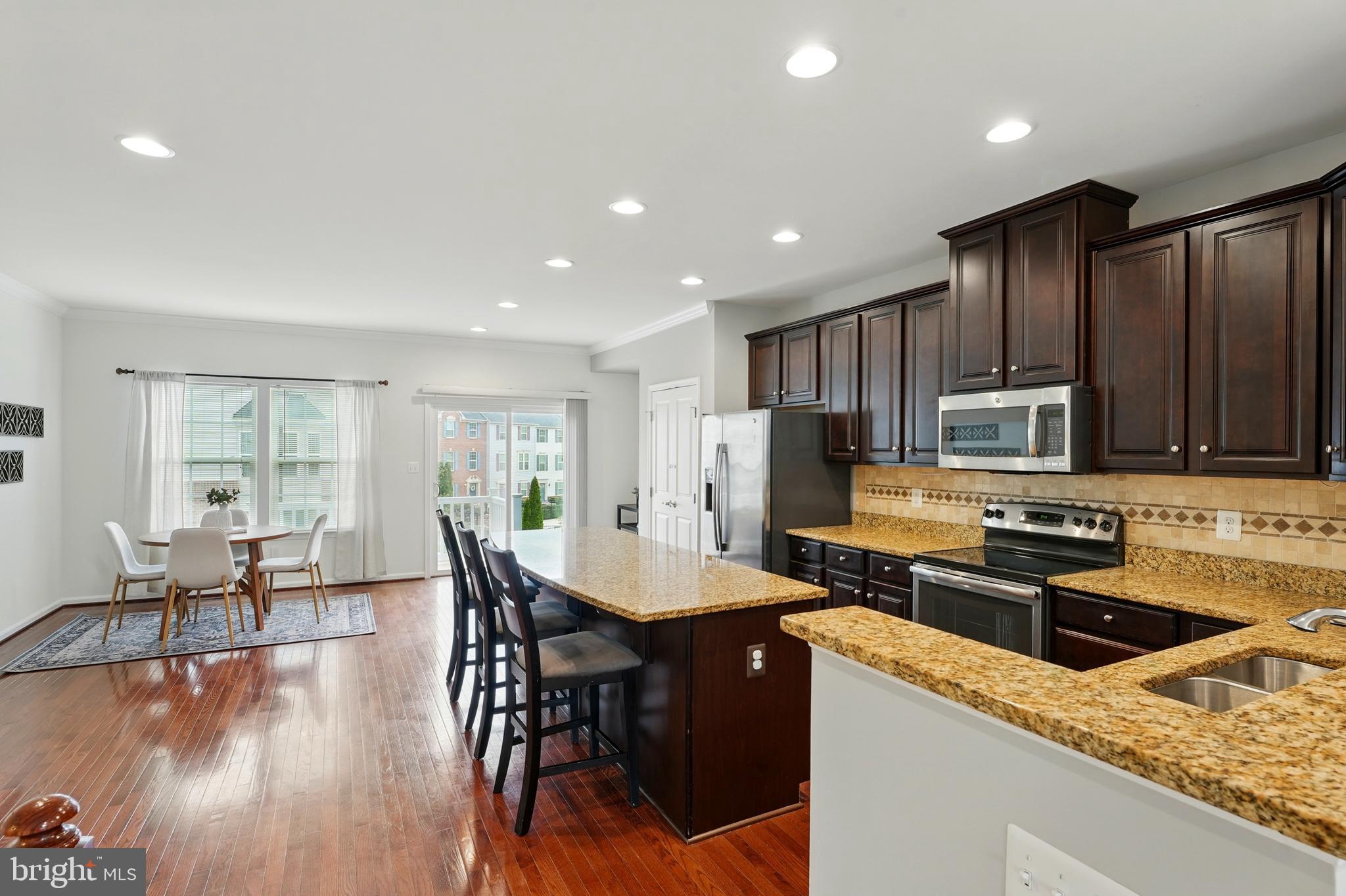 7054 Kona Drive Gainesville, VA 20155 - Photo 12 of 39 a kitchen with granite countertop a stove a sink a microwave a dining table and chairs