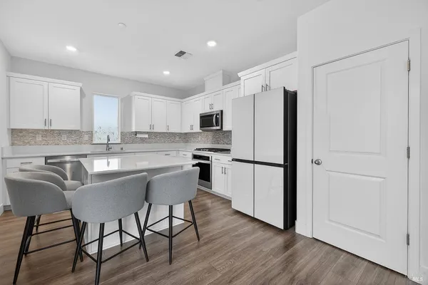 a kitchen with stainless steel appliances granite countertop a refrigerator a stove a sink and white cabinets with wooden floor