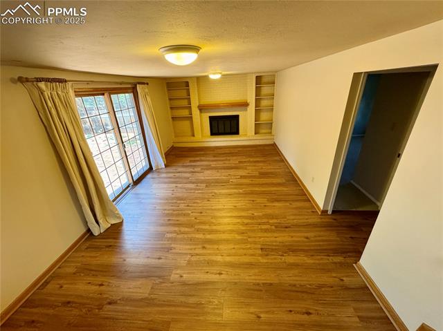 280 Raven Hills Road Colorado Springs, CO 80919 - Photo 40 of 48 Unfurnished living room with a textured ceiling, a fireplace, built in shelves, wood finished floors, and baseboards