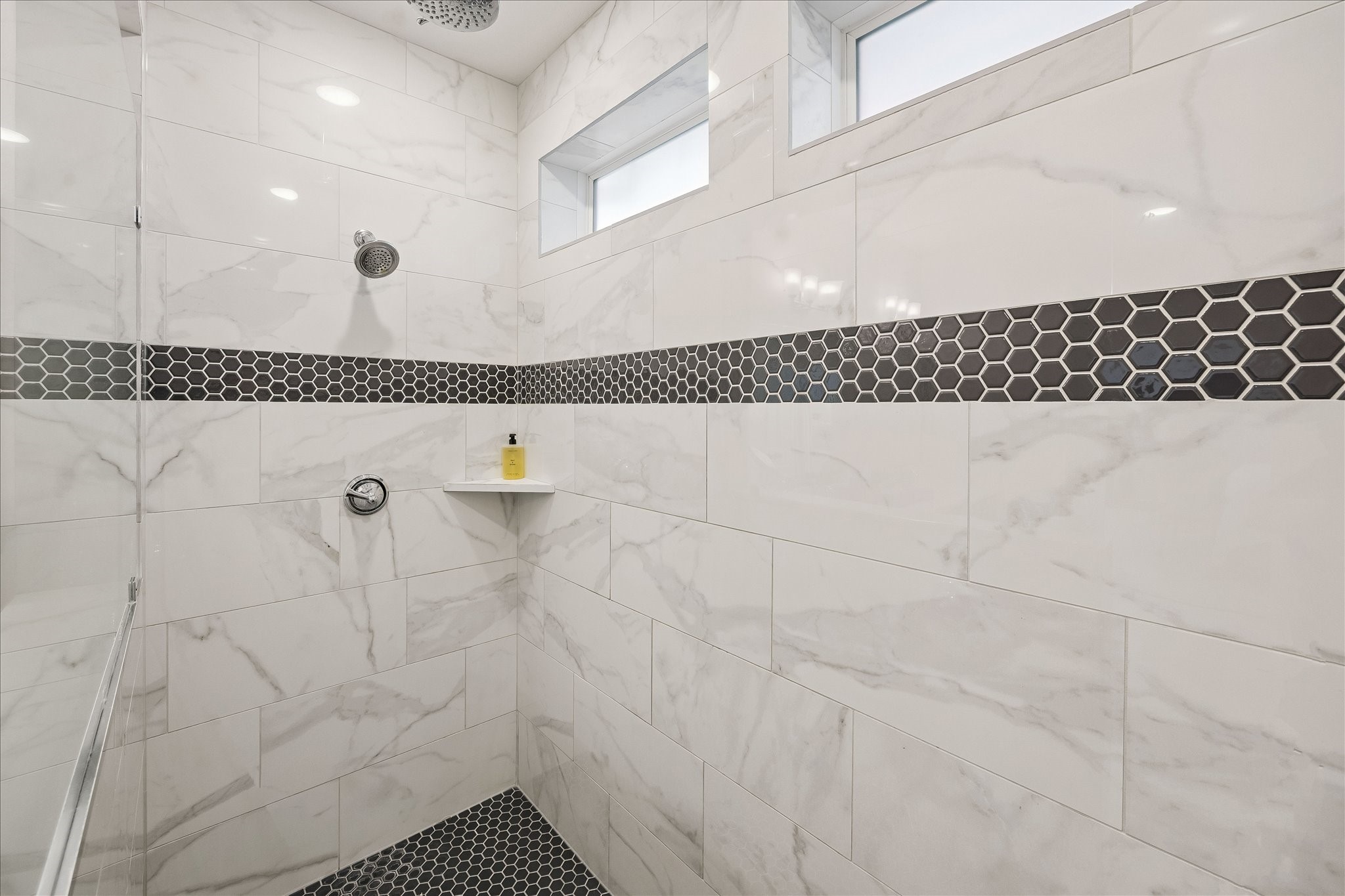 2512 Swang Pl. Houston, TX 77008 - Photo 26 of 46 This modern shower features elegant tile with a stylish hexagonal accent strip. It includes a rainfall showerhead, built-in corner shelf, and small upper windows for natural light.