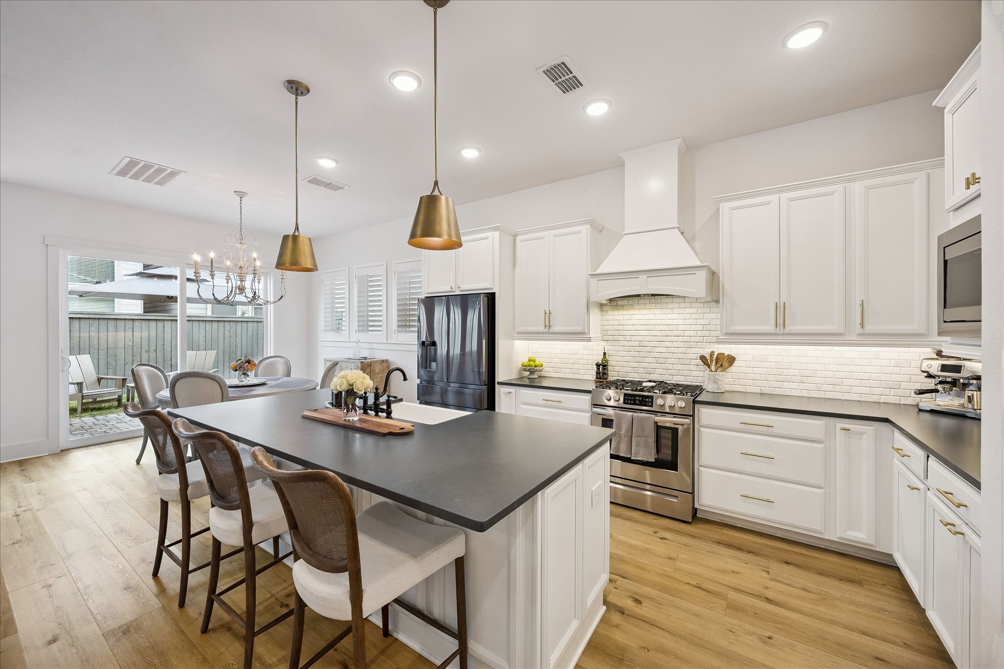 2512 Swang Pl. Houston, TX 77008 - Photo 7 of 46 This modern kitchen features sleek cabinetry, stainless steel appliances, and a large island with seating. The space is brightened by recessed lighting and pendant lamps, and opens to an outdoor area, creating an inviting and functional atmosphere.