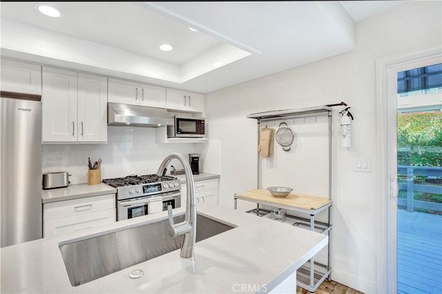 a kitchen with stainless steel appliances granite countertop a stove top oven a sink a refrigerator and white cabinets with wooden floor