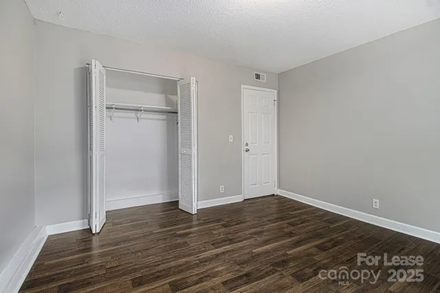 a view of an empty room with wooden floor & closet