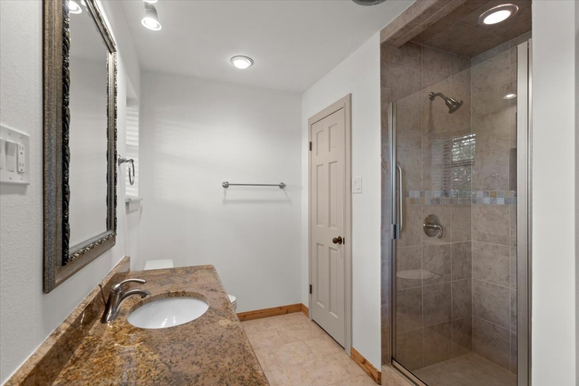 16808 Forest Way Austin, TX 78734 - Photo 17 of 33 a bathroom with a granite countertop sink a mirror a shower and vanity