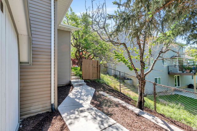 3813 North Foothill Drive Provo, UT 84604 - Photo 49 of 71 Concrete pathway leading to a wooden fence, bordered by a textured siding exterior and mulched landscaping