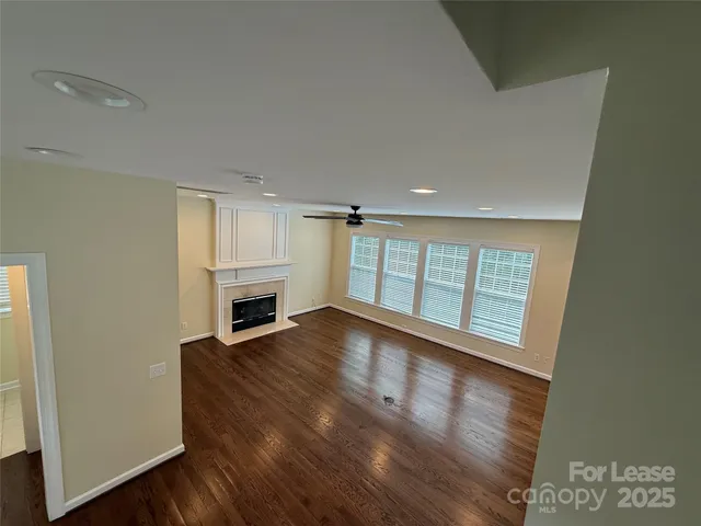 an empty room with wooden floor fireplace and windows