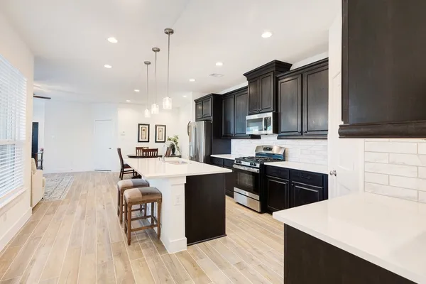 a kitchen with stainless steel appliances kitchen island granite countertop a stove top oven a sink dishwasher and a refrigerator with wooden floor