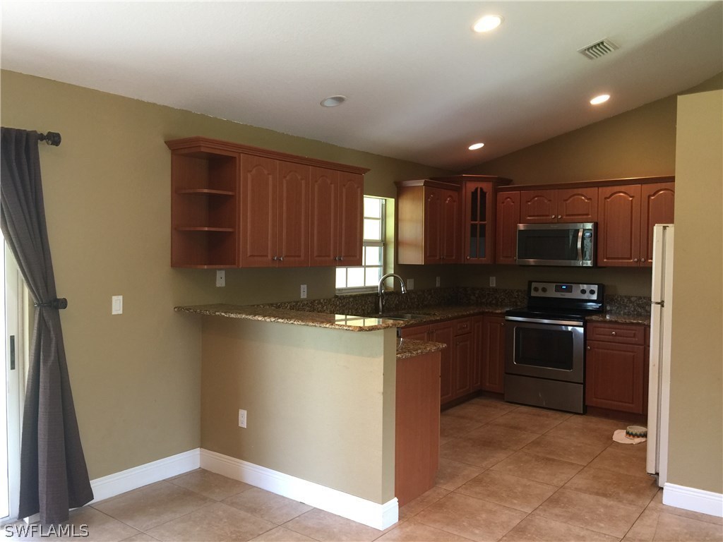 4015 36th Street Southwest Lehigh Acres, FL 33976 - Photo 7 of 23 a kitchen with stainless steel appliances granite countertop a refrigerator and a stove top oven