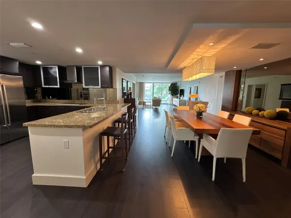 a large dining hall with stainless steel appliances granite countertop a stove a sink a dining table chairs and couches with wooden floor