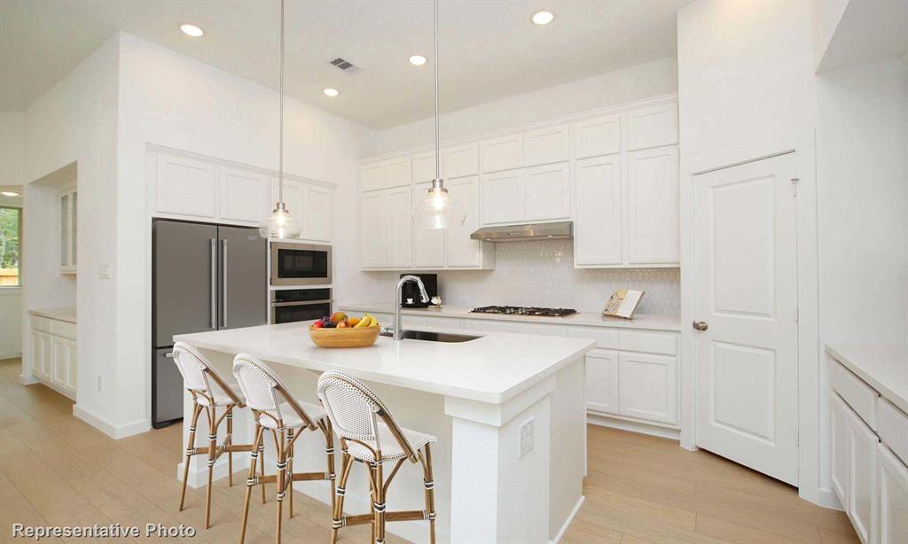 a kitchen with stainless steel appliances a stove a sink a refrigerator and white cabinets with wooden floor