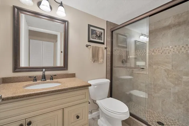 a bathroom with a granite countertop toilet a sink a mirror a vanity and shower
