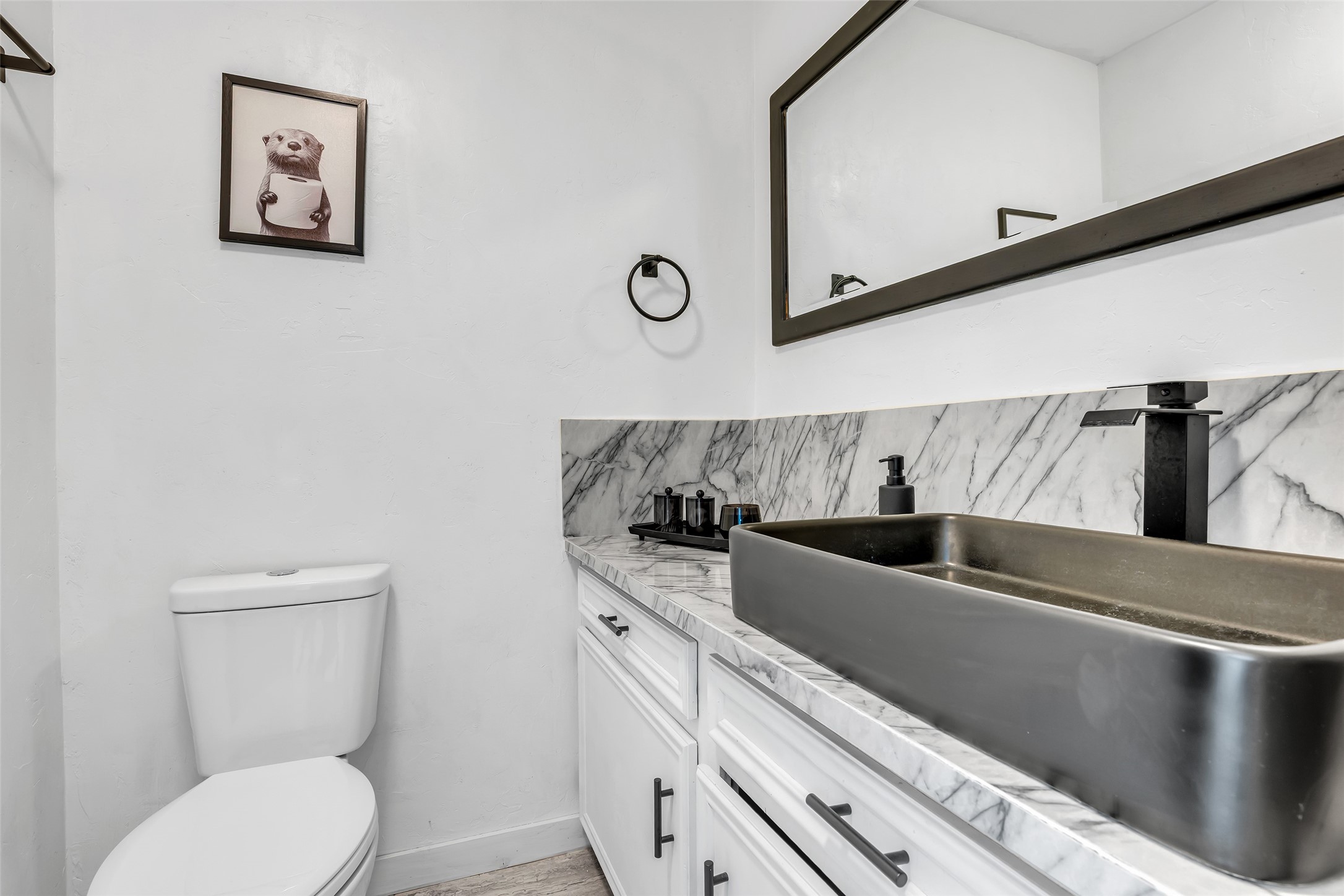 22502 Fields Lane Spring, TX 77389 - Photo 29 of 39 This complete bathroom features a modern design with a sleek black sink, marble countertop, and a large framed mirror. The white walls and cabinetry create a bright and clean look, complemented by a playful framed picture.