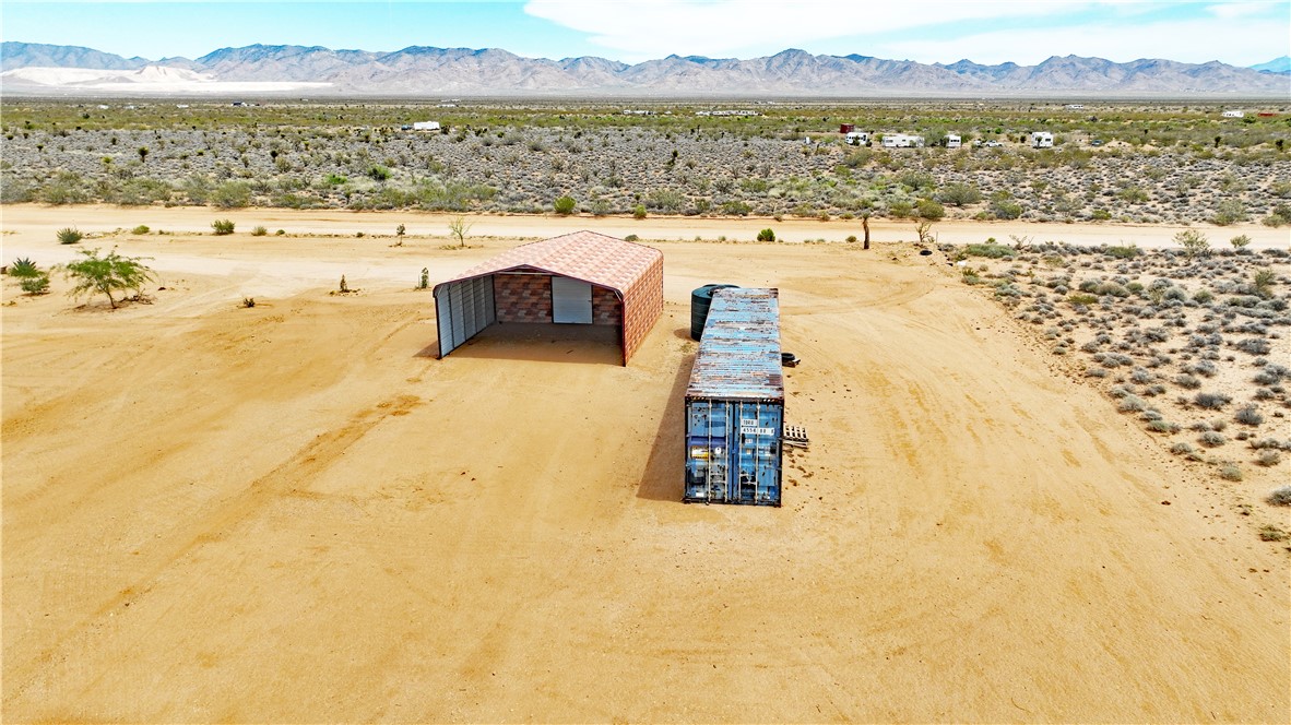 5649 Davis Road Golden Valley, AZ 86413 - Photo 4 of 24 Expansive desert landscape featuring a metal-frame structure with a brick-patterned facade, a blue cargo container, and distant mountains under a blue sky