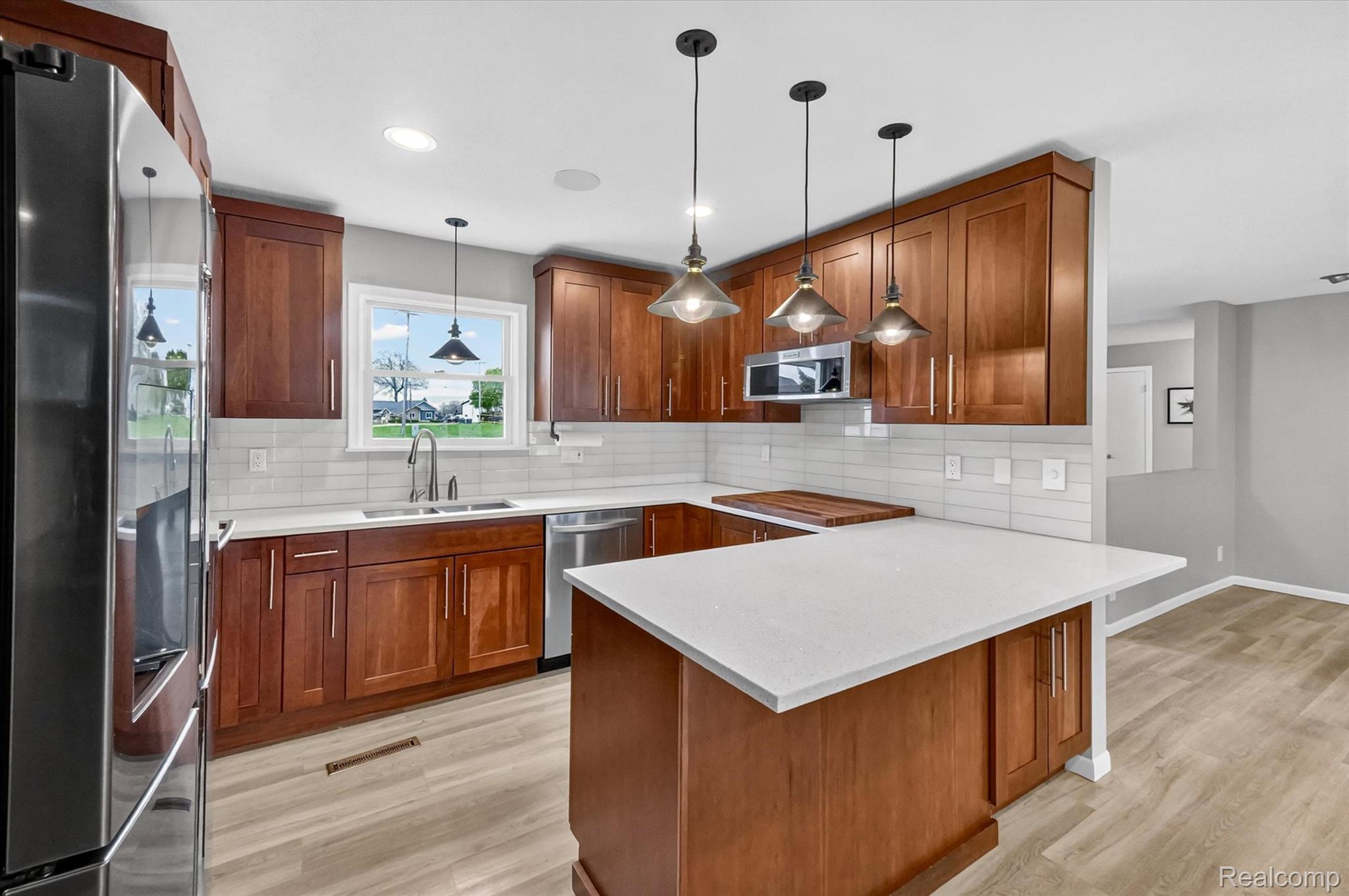 2264 Crane Road Fenton, MI 48430 - Photo 15 of 55 Kitchen with stainless steel appliances, a peninsula, wood finish cabinetry, light wood-style floors, and light stone countertops