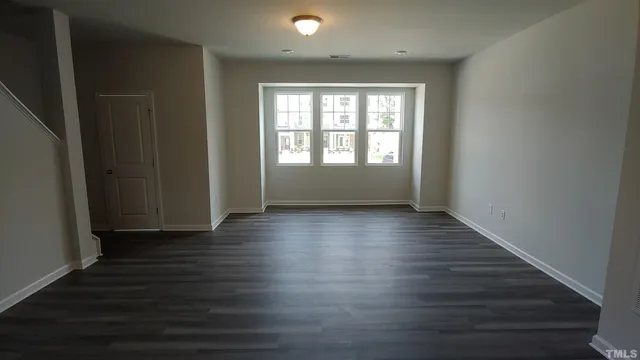 an empty room with wooden floor and windows with curtains