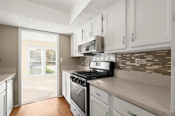 a kitchen with stainless steel appliances granite countertop white cabinets a window and a sink