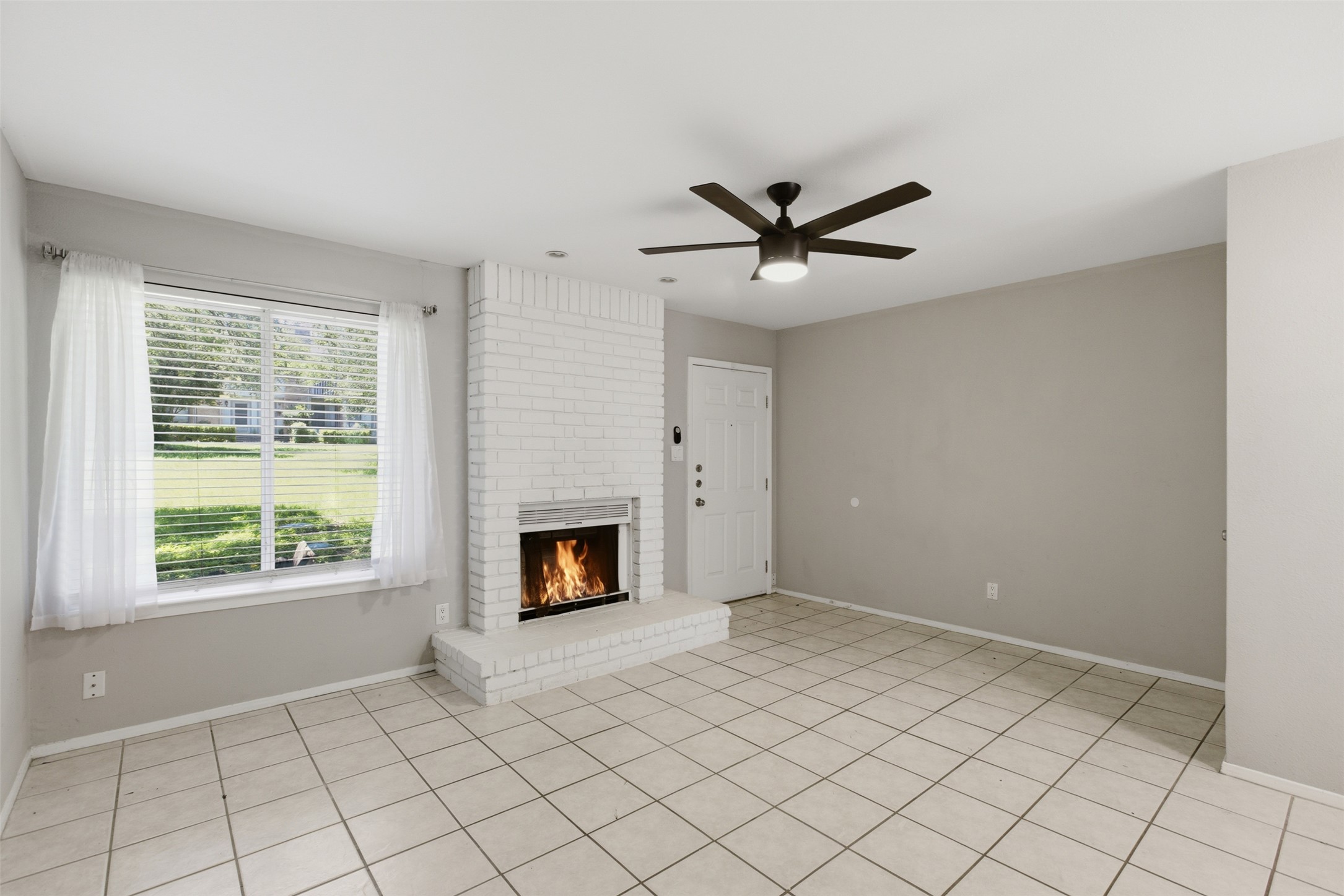 4204 Hudson Bend Road, Unit B Austin, TX 78734 - Photo 2 of 37 Spacious living area featuring a prominent brick fireplace with a hearth, tile flooring, and a large window overlooking exterior greenery