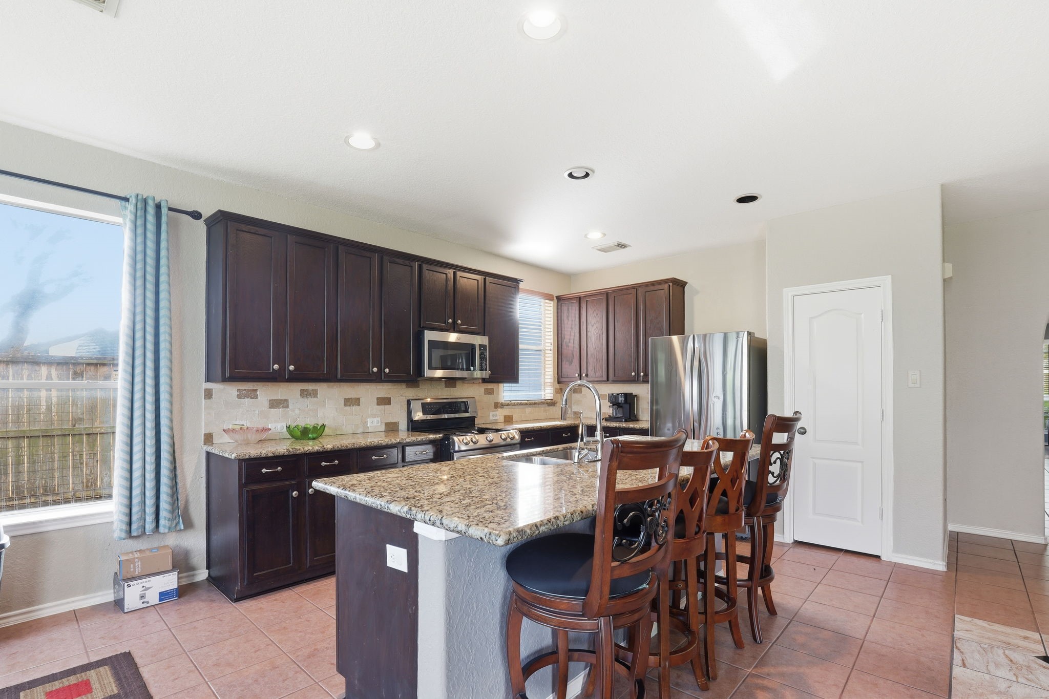 8202 Terrace Brook Drive Houston, TX 77040 - Photo 13 of 23 This kitchen features dark wood cabinetry, stainless steel appliances, and a spacious granite island with seating. It has a modern tile backsplash, ample natural light, and an open layout ideal for entertaining.