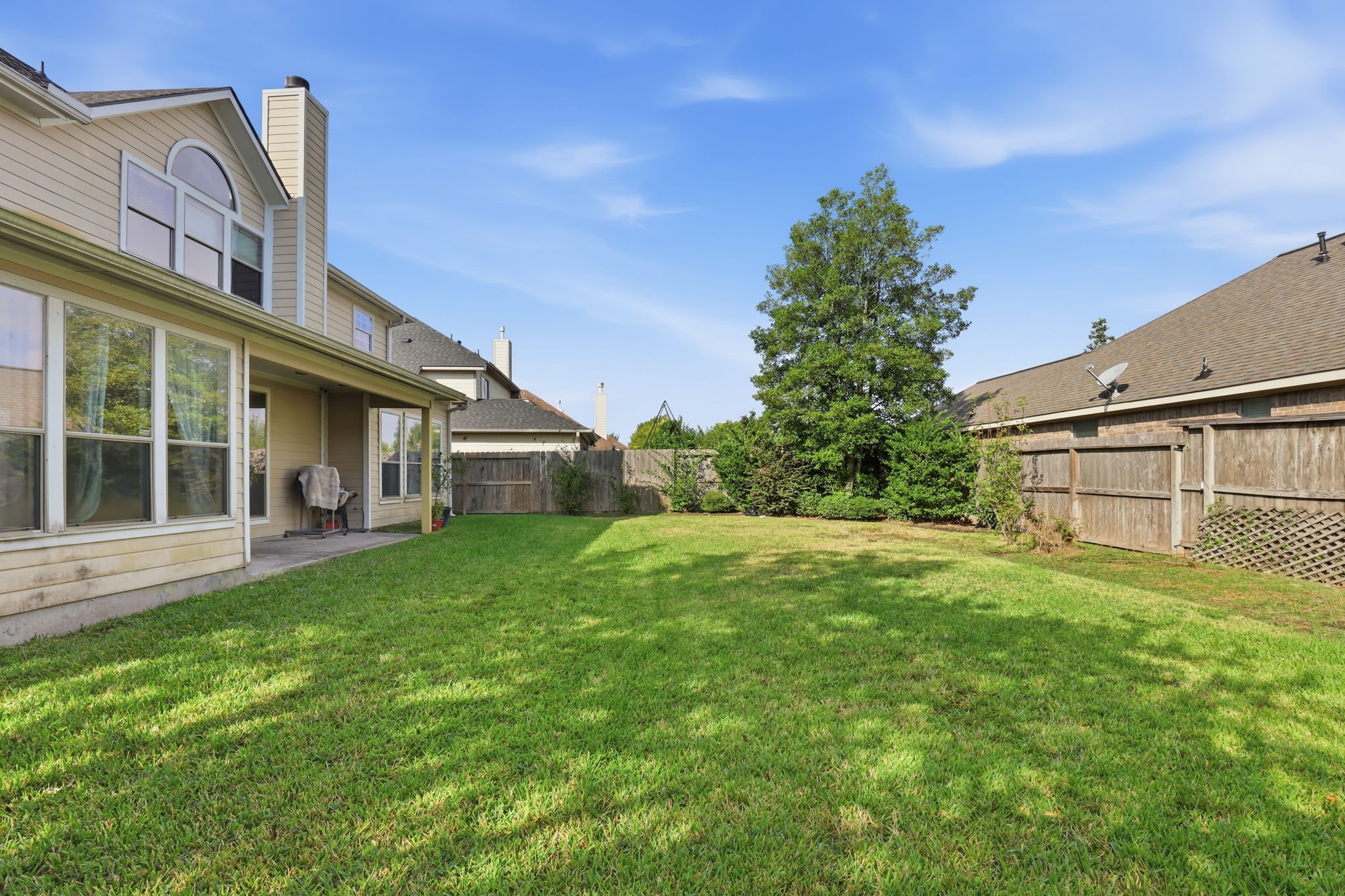8202 Terrace Brook Drive Houston, TX 77040 - Photo 22 of 23 Spacious backyard with lush green lawn, bordered by a wooden fence. The house has large windows and a covered patio area, ideal for outdoor relaxation.