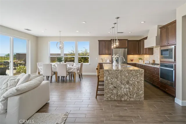 a kitchen with stainless steel appliances kitchen island granite countertop a refrigerator a stove a sink a dining table and chairs with wooden floor