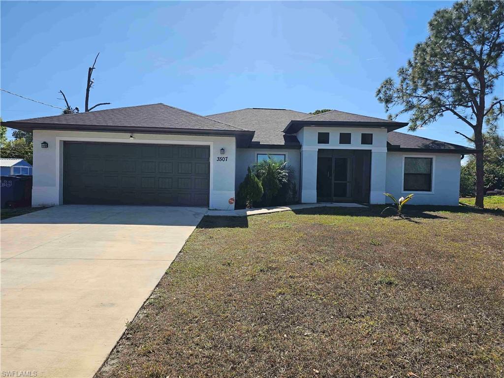 3507 2nd Street Southwest Lehigh Acres, FL 33976 - Photo 9 of 27 Prairie-style home with stucco siding, a front yard, concrete driveway, a garage, and roof with shingles