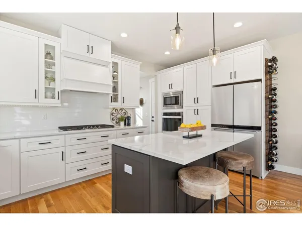 a kitchen with stainless steel appliances kitchen island granite countertop a stove a sink dishwasher and white cabinets with wooden floor