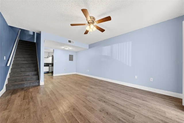 a view of an empty room with wooden floor and a ceiling fan