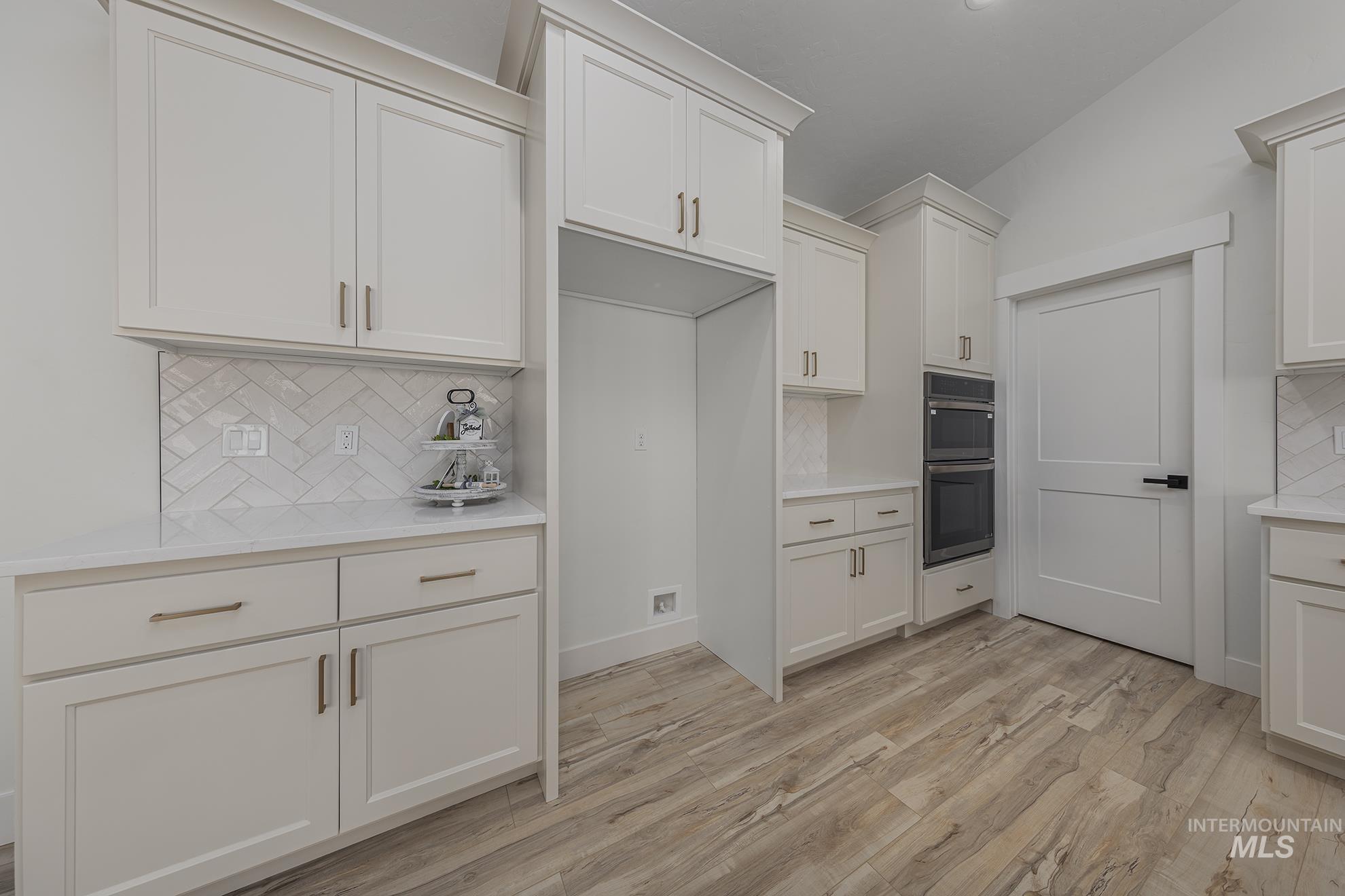 2810 Cypress Point Payette, ID 83661 - Photo 5 of 46 Kitchen featuring decorative backsplash, light wood-style flooring, stainless steel double oven, white cabinets, and light stone counters