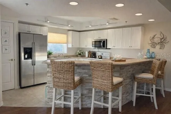 a kitchen with stainless steel appliances granite countertop a stove a sink a refrigerator white cabinets and chairs