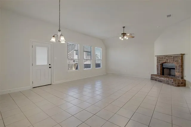 an empty room with chandelier fan and kitchen view
