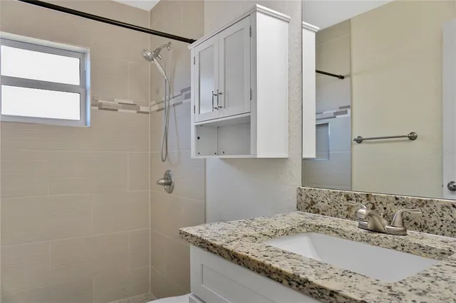 a bathroom with a granite countertop sink a mirror and shower
