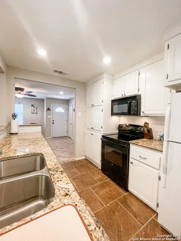 a large kitchen with granite countertop a sink and white cabinets
