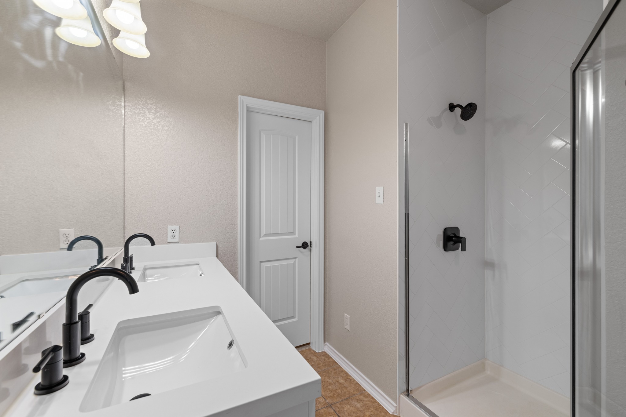 403 Red Hawk Drive Leander, TX 78641 - Photo 18 of 37 Bathroom featuring a double vanity with integrated sinks, matte black fixtures, an expansive mirror, and a glass-enclosed shower with white herringbone tile