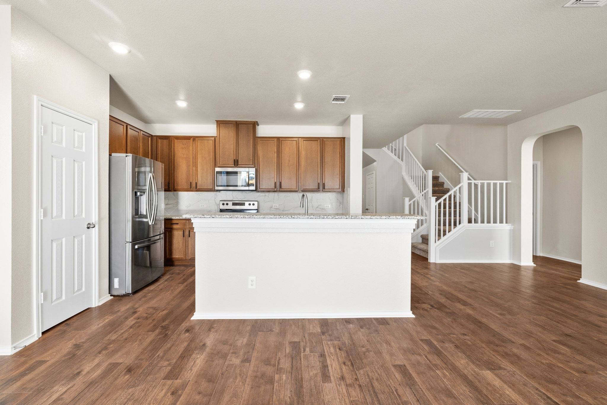 1829 Stringer Pass Leander, TX 78641 - Photo 11 of 36 Kitchen with stainless steel appliances, arched walkways, a center island, wood finish cabinets, and dark wood-type flooring