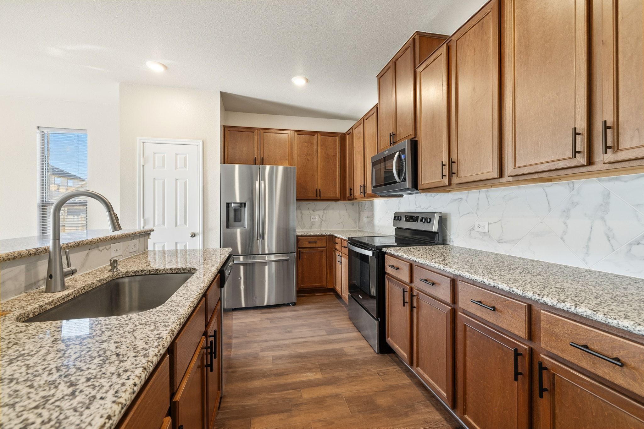 1829 Stringer Pass Leander, TX 78641 - Photo 12 of 36 Kitchen with stainless steel appliances, wood finish cabinets, dark wood-style floors, light stone countertops, and decorative backsplash