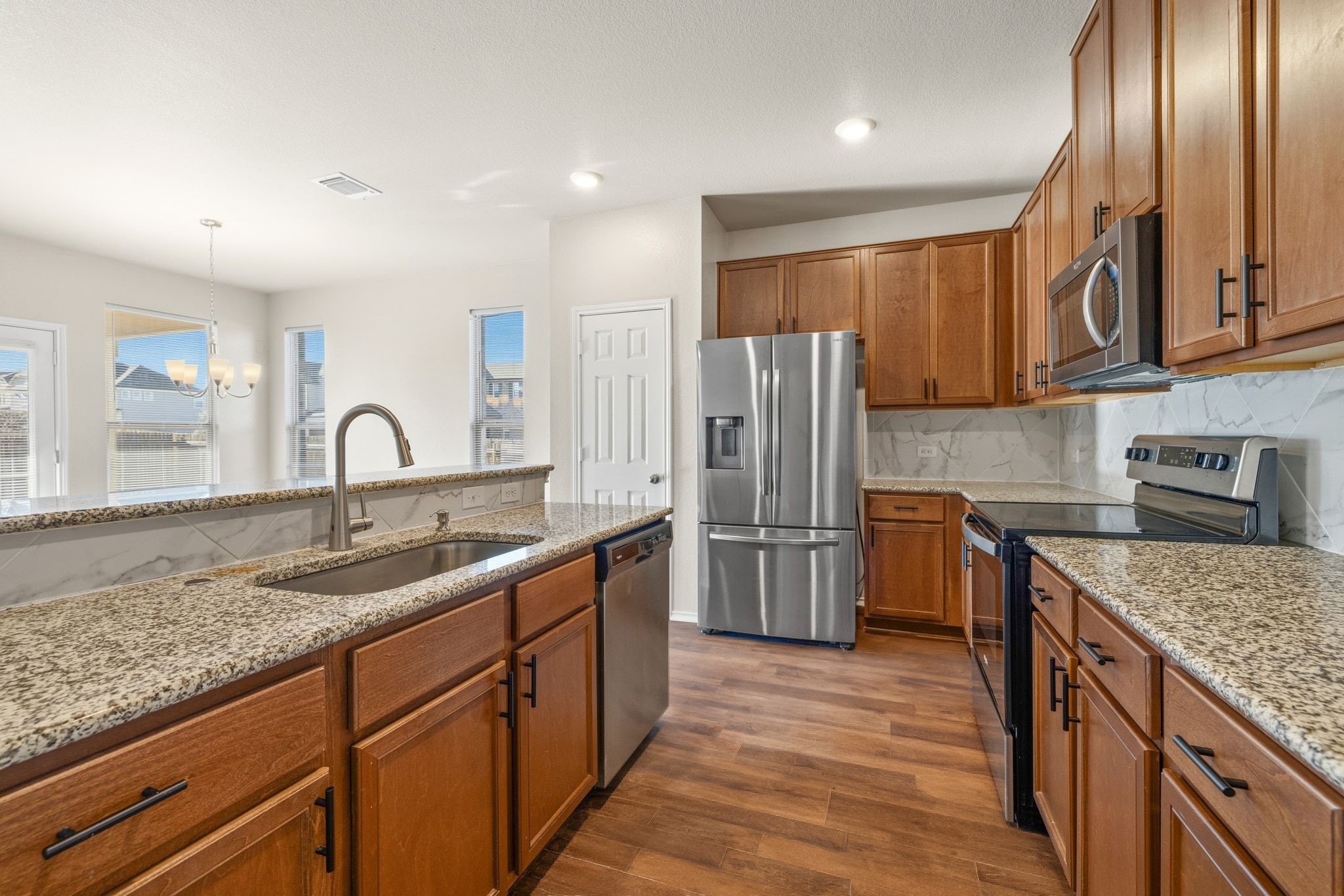 1829 Stringer Pass Leander, TX 78641 - Photo 13 of 36 Kitchen featuring wood finish cabinetry, stainless steel appliances, dark wood finished floors, and light stone counters