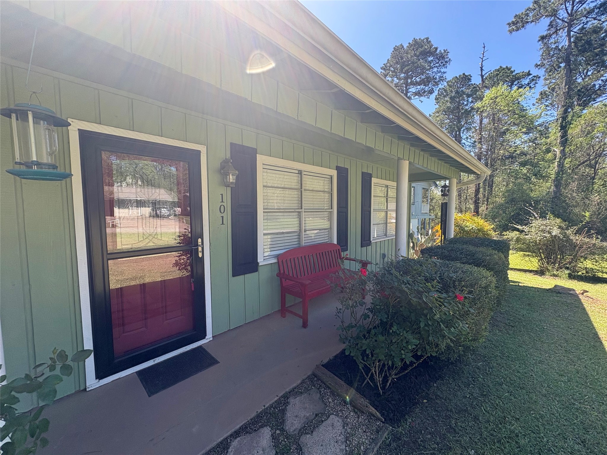 101 Pine Shadows Lane Coldspring, TX 77331 - Photo 2 of 10 Charming home with a welcoming front porch, featuring a red bench and lush greenery. The exterior is accented with a storm door, and the surrounding trees offer a serene, natural backdrop.