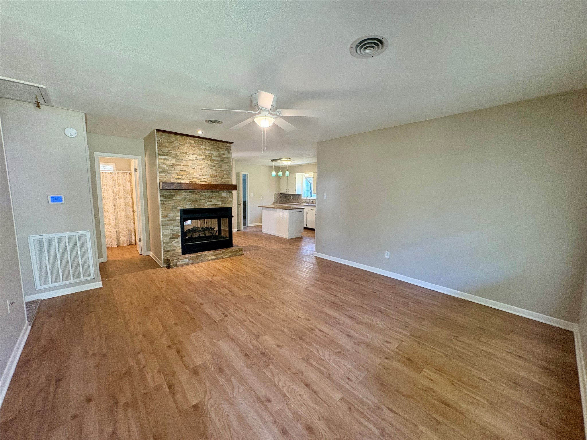 101 Pine Shadows Lane Coldspring, TX 77331 - Photo 3 of 10 This spacious living area features warm wood vinyl flooring and a cozy propane stone fireplace. It flows seamlessly into an open kitchen with modern lighting. Ceiling fans provide comfort, and neutral walls offer a versatile backdrop for any decor style.