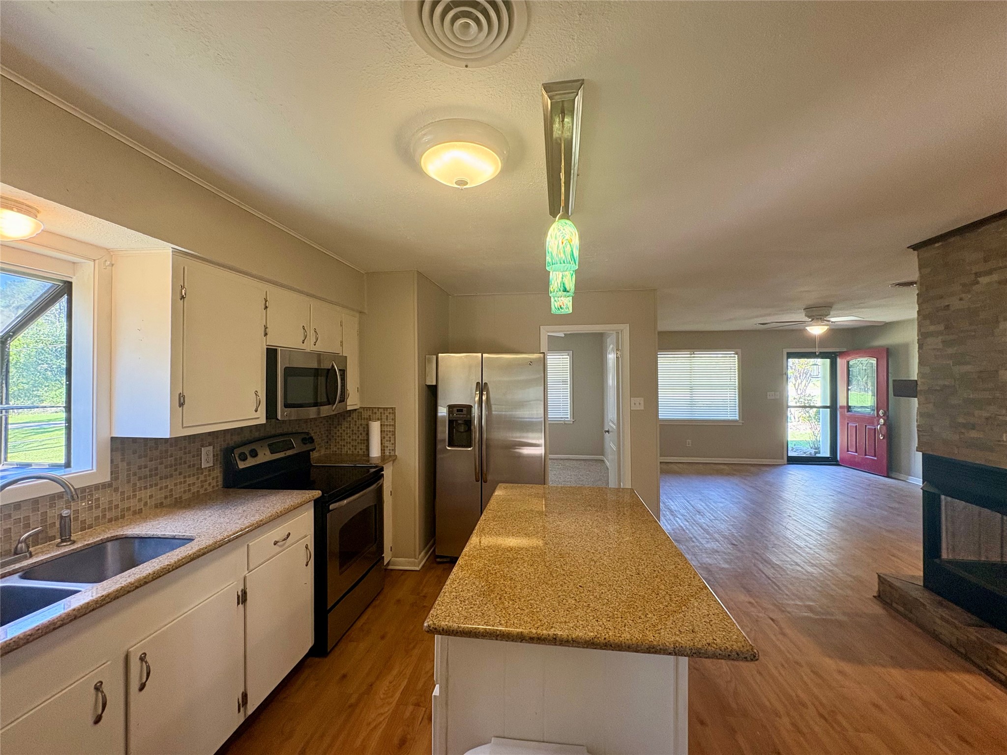 101 Pine Shadows Lane Coldspring, TX 77331 - Photo 5 of 10 This open-concept kitchen and living area features modern stainless appliances, island and granite countertops. The kitchen island provides extra workspace, while large windows and a glass front door offer plenty of natural light. A stone-accented fireplace adds a cozy touch.