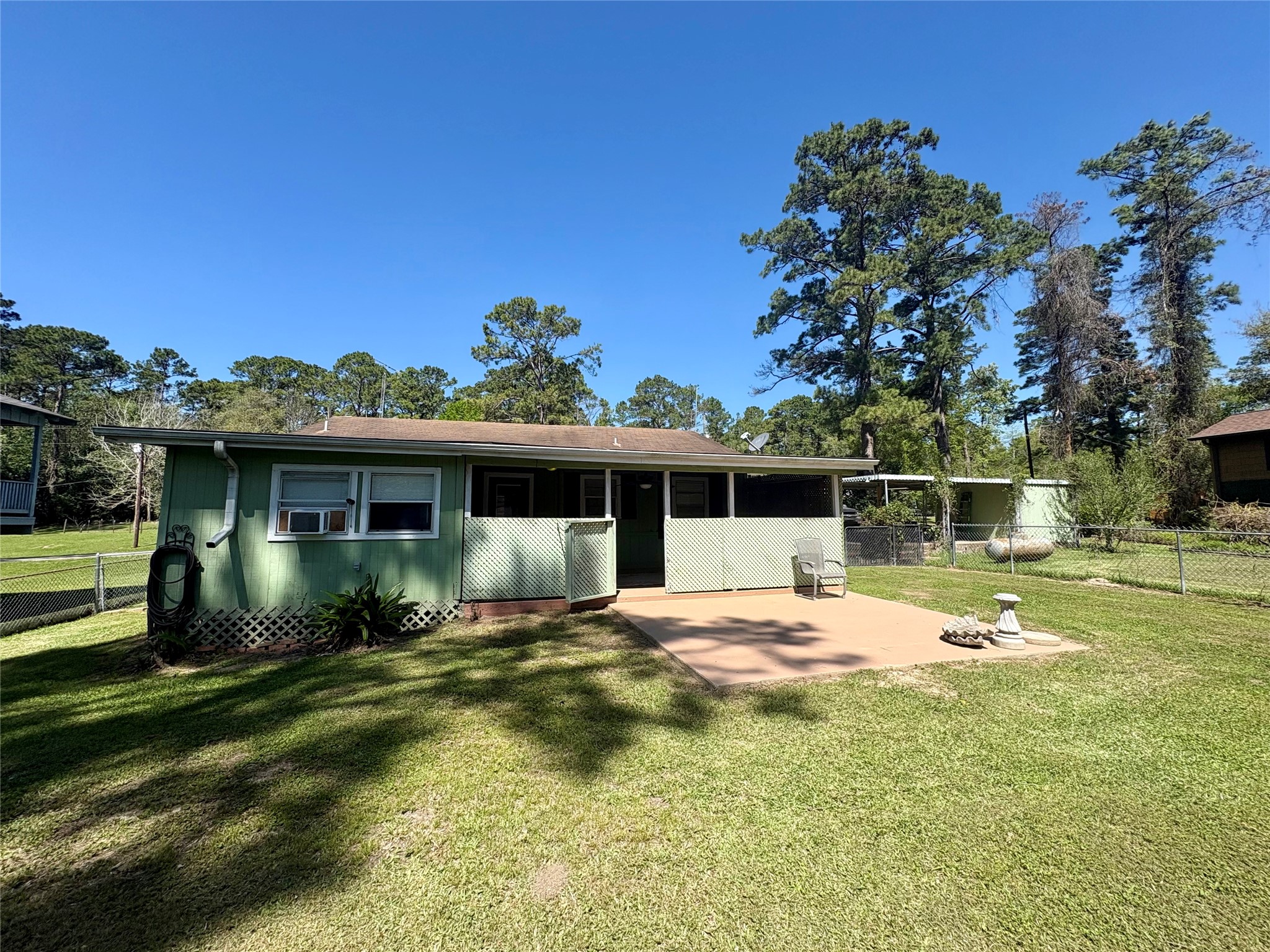 101 Pine Shadows Lane Coldspring, TX 77331 - Photo 8 of 10 Charming home with a spacious fenced backyard, patio area, and surrounded by tall trees, offering a serene outdoor setting.
