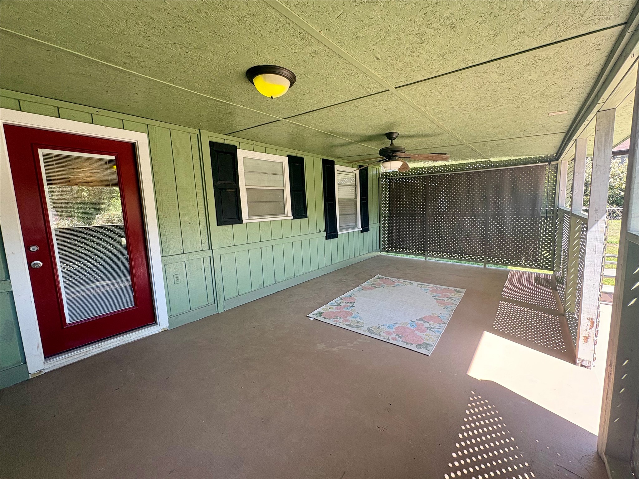 101 Pine Shadows Lane Coldspring, TX 77331 - Photo 9 of 10 This is a spacious screened porch with a green exterior, red door, and ceiling fan. It features lattice privacy panels and offers a cozy outdoor space perfect for relaxation.