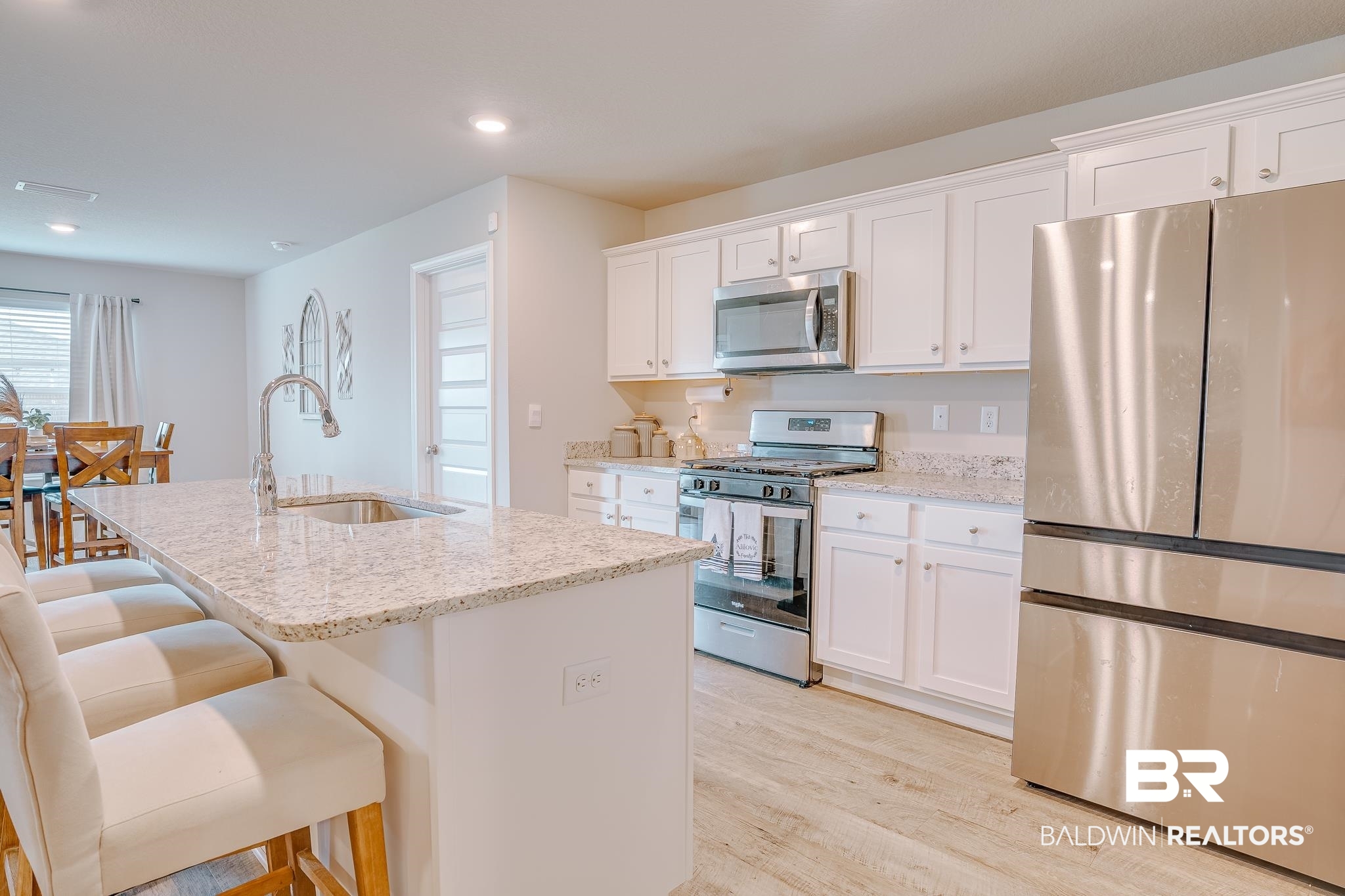 8242 Sycamore Way Semmes, AL 36575 - Photo 14 of 43 Kitchen featuring appliances with stainless steel finishes, light wood-style flooring, an island with sink, light stone counters, and white cabinetry