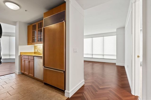 a view of a refrigerator in kitchen and an empty room with wooden floor windows