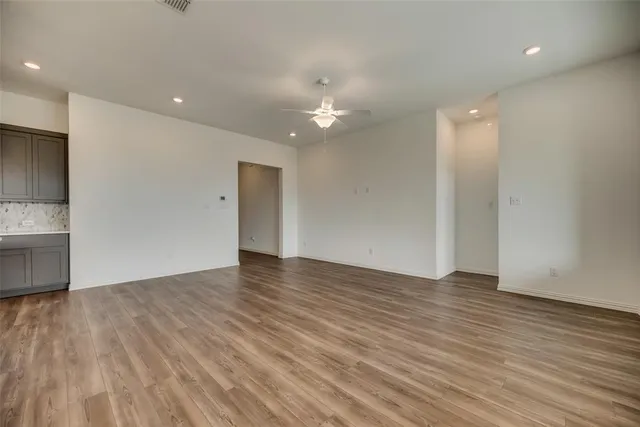 a view of an empty room with wooden floor and a kitchen