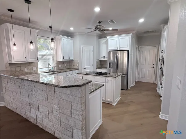 a kitchen with kitchen island granite countertop a sink refrigerator and cabinets