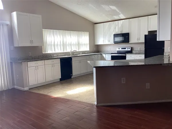 a kitchen with stainless steel appliances granite countertop a stove top oven a sink dishwasher and a refrigerator with wooden floor