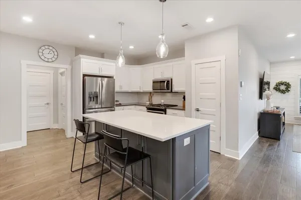 a kitchen with kitchen island a refrigerator a stove a microwave oven a sink with island and chairs with wooden floor