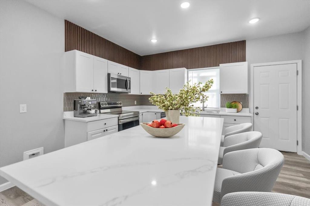 3512 Hamilton Avenue Dallas, TX 75210 - Photo 7 of 23 Kitchen featuring a kitchen bar, light wood-type flooring, appliances with stainless steel finishes, white cabinets, and light stone countertops