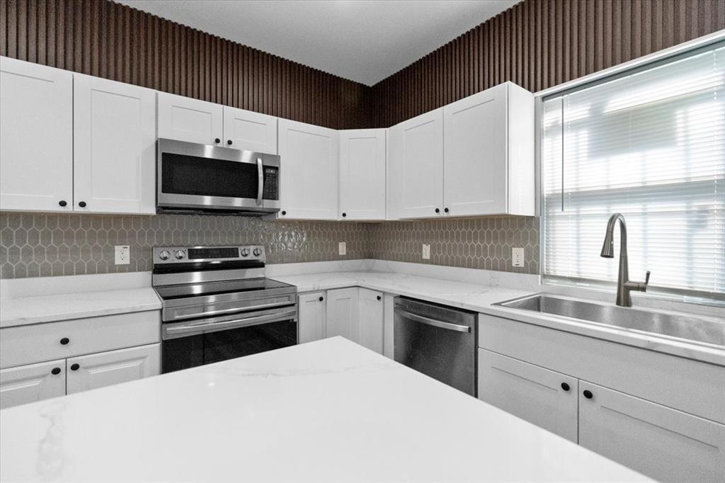 3512 Hamilton Avenue Dallas, TX 75210 - Photo 8 of 23 Kitchen featuring wallpapered walls, appliances with stainless steel finishes, white cabinets, and light stone countertops
